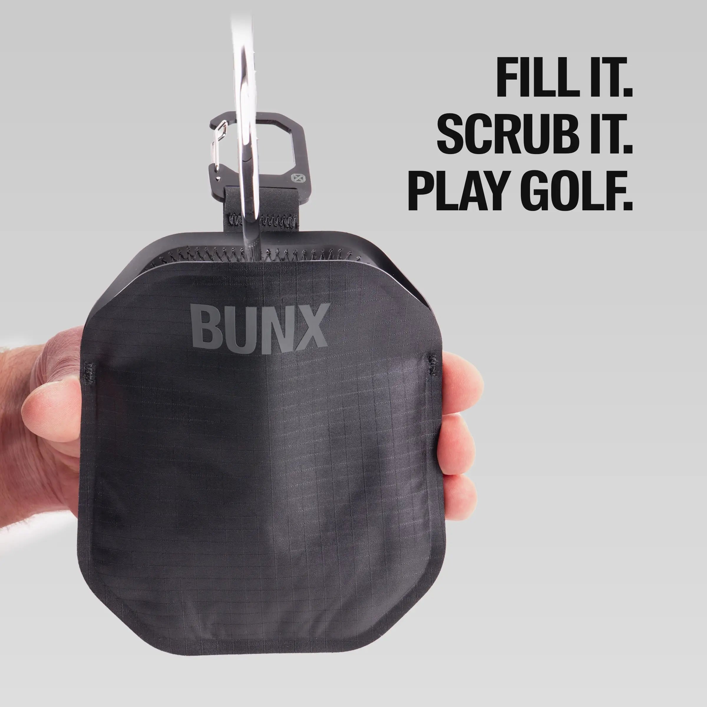 Hand holding black BUNX Golf Scrub Pouch by stainless carabiner showing compact size